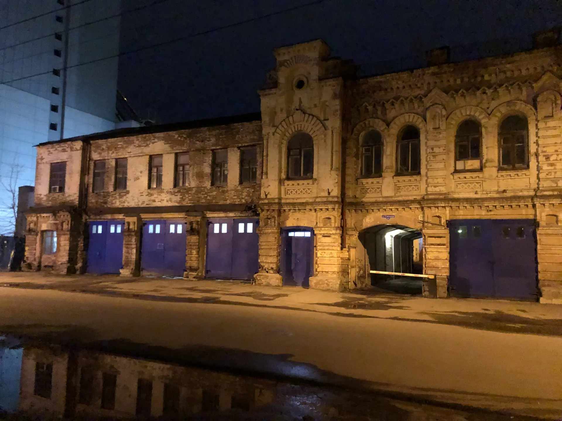 Старый кирпичный дом ночью, отражающийся в мокрой дороге